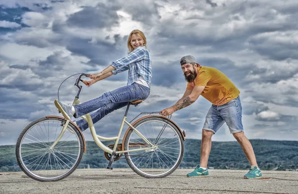 Женщина ездит на велосипеде небо фоне. Человек помогает поддерживать равновесие и ездить на велосипеде. Как научиться ездить на велосипеде, как взрослый. Девушка катается на велосипеде, пока ее поддерживает парень. Велосипедная техника. Обучение велоспорту при поддержке — стоковое фото