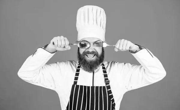 Låt oss prova maträtt. Hungrig kock redo att prova mat. Dags att smaka. Chef glad leende ansikte hålla sked och gaffel. Man stilig med skägg håller köksutrustning på blå bakgrund. Koncept för matlagningsprocess — Stockfoto