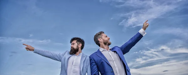 Men formal suit managers pointing at opposite directions. Changing course. New business directions. Developing business direction. Businessmen bearded faces stand back to back sky background