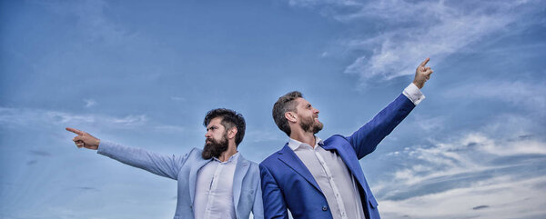 Мужчины в костюмах указывают на противоположные стороны. Меняю курс. Новые направления бизнеса. Развитие бизнес-направления. Бизнесмены с бородой стоят спиной к небу
