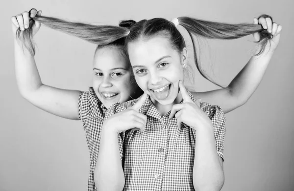 Si prende cura dei suoi capelli. Ragazzina giocosa che tiene i capelli lunghi del bambino adorabile. Ragazzo carino felice con code di cavallo di capelli alla moda. Bambino piccolo sorridente con i capelli biondi — Foto Stock