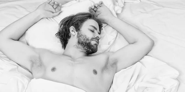 Obrázek ukazuje mladý muž v posteli. Mladý muž táhnoucí se při probuzení v dopoledních hodinách. Muž s očima stále uzavřen dosahující tlačítko na hodiny jej vypnout. — Stock fotografie