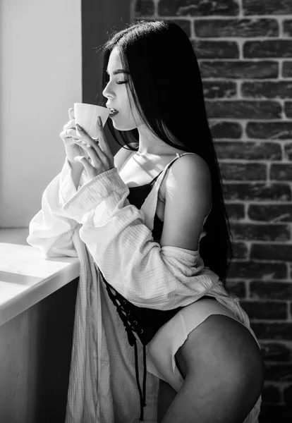 Lingerie feminina atraente relaxante em casa. Apaixonado amante misterioso. Hora perfeita do café. Mas primeiro café. A desfrutar da luz solar da manhã. Sensual menina sexy seios beber café perto do peitoril da janela — Fotografia de Stock