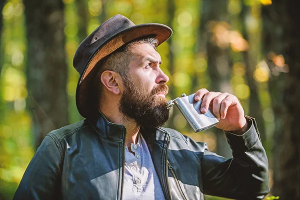 L'uomo nomade porta con sé dell'alcol. Un tizio barbuto e brutale beve una fiaschetta alcolica di metallo. Hipster con barba bere alcolici sfondo natura sfocato. L'avventura inizia dal primo sorso. Bevanda alcolica — Foto Stock