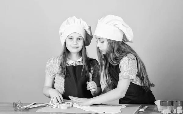 Giovani panettieri seguendo la ricetta di cottura. Piccoli panettieri rotolamento pasta sul tavolo della cucina. Bambine che cucinano biscotti in panetteria. Impastare l'impasto con farina da forno — Foto Stock