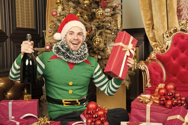 Papai Noel e presentes de Natal conceito. Homem usar roupas de elfo santa chapéu celebrar Natal interior decorado abeto e presentes. Bebida de champanhe de Natal. Homem comemorar ano novo ou feriado de Natal — Fotografia de Stock