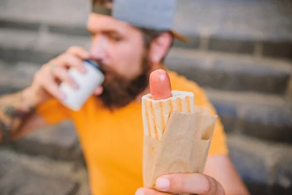 Hot dog sausage in bun. Bearded man eating unhealthy hot dog sandwich. Hipster drinking coffee with hot dog during rest break. Caucasian guy enjoying hot dog traditional street cuisine