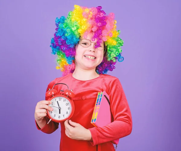 Life is fun. Happy childhood. Happy little girl. International childrens day. Child care. Happy moments. Kid hold alarm clock. Girl cute playful kid wear curly rainbow wig. Take care of your time