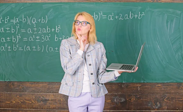 Woman wear eyeglasses holds laptop surfing internet. Educator smart clever lady with modern laptop searching information chalkboard background. Online schooling concept. Educational site for teachers Stock Picture