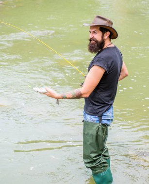 Balık tutmanın eğlencesi yakalamaktır. Balıkçı ekipmanları ile Fisher. Kancadaki balıklar. Vahşi doğada eğlence. Balıkçılık erkeksi hobi. Acımasız adam nehir suyunda dikilir lastik çizmeler giyer. Fisher hafta sonu etkinliği