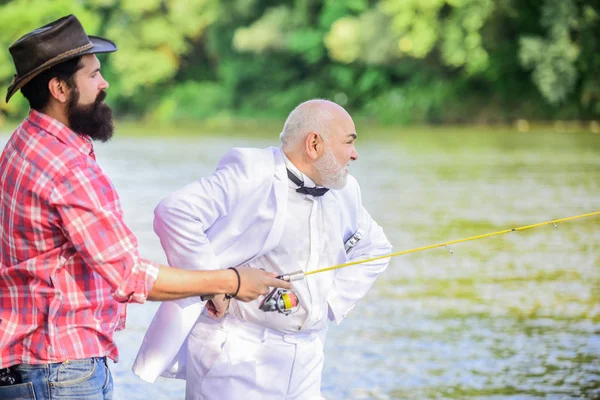 Expert fisherman. Bearded man elegant businessman fish together. Learn to fish. Fishing skills. Fish with companion who help in emergency. Men friends relaxing river background. Personal instructor