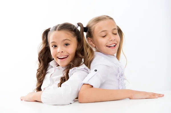 Feliz infancia. Adorables colegialas. De vuelta a la escuela. Concepto educativo. Hermosas chicas mejores amigas. Estilo formal. Las colegialas se sientan en el escritorio fondo blanco. Colegialas amigos emocionales — Foto de Stock