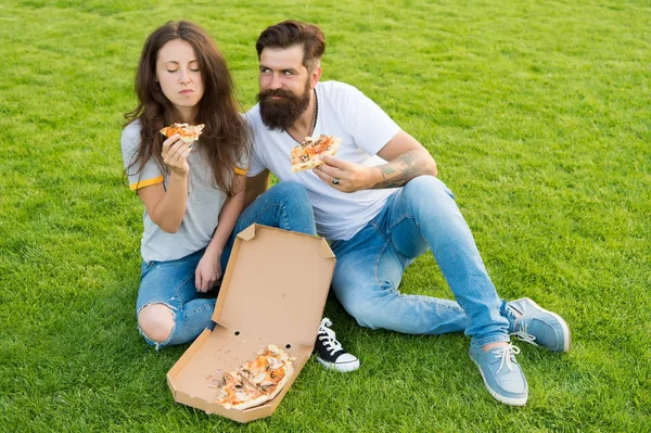 Pizza lovers. happy couple eating pizza. couple in love dating. fast food. bearded man hipster and adorable girl eat pizza. family weekend. summer picnic on green grass — Stock Photo, Image