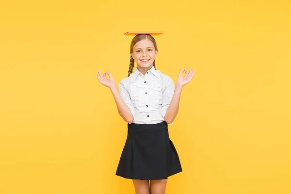 Ein Ort, an dem man sich zentrieren kann. zurück zur Schule. Schüler im Buchladen oder in der Schulbibliothek. Kinderyoga-Literatur. Meditieren. glückliche Mädchen lernen hart mit Notizbuch. kleines Mädchen mit Buch auf dem Kopf — Stockfoto