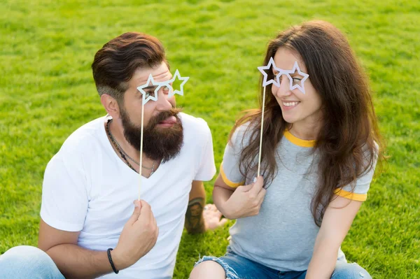Enjoying funny photo booth. Funny couple looking through prop glasses on green grass. Bearded man and sexy woman making funny grimace on summer day. Funny and playful