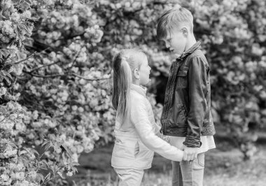 Aşık olmak için bahar zamanı. Pembe kiraz çiçeğine aşık çocuklar. Havada aşk var. Çift sevimli sevimli çocuklar sakura bahçe yürümek. Şefkatli aşk duyguları. Küçük kız ve oğlan. Parkta romantik tarih