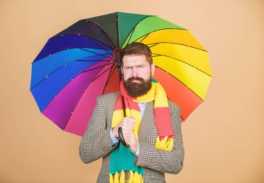 Sakallı adam renkli şemsiye tutuyor. Yağmur yağıyor gibi görünüyor. Yağmurlu günleri atlatmak zor olabilir. Yağmurlu bir güne hazır olun. Kaygısız ve olumlu. Yağmurlu günün tadını çıkar. Gelecekteki hava eğilimlerini tahmin et