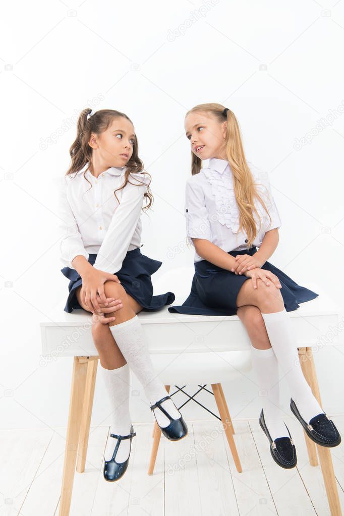 Competitors. Every day better. Little schoolgirls classmates friendly kids. Schoolgirls friends sit on desk. Best friends relaxing. Schoolgirls tidy hairstyle relaxing having rest. School uniform
