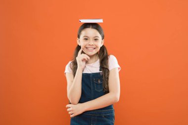 Kafasına kitap. Uyum içinde. Küçük bir kız elinde ders kitabı kafası tutuyor. Küçük kız kitap turuncu arka plan. Çocuk için ilginç bir hikaye. Çalışmak ve dinlenmek. Motivasyon ve ilham. Bakiyeyi bulma