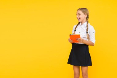 İyi bilginin neşesi. Sarı arka plan üzerine kitap tutan sevimli küçük bir kız. Kitaptan bilgi alan sevimli küçük okul çocuğu. Bilgi ve beceriler. Bilgi günü veya 1 Eylül, boşluğu kopyala