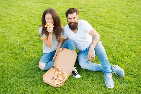 They are sharing pizza and eating. couple in love dating. family weekend. fast food. bearded man hipster and adorable girl eat pizza. happy couple eating pizza. summer picnic on green grass