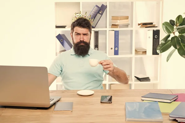 King of office. Head of department. Head office concept. Man bearded manager businessman entrepreneur wear golden crown on head. Relaxed top manager drinking coffee. Confident boss enjoying his glory