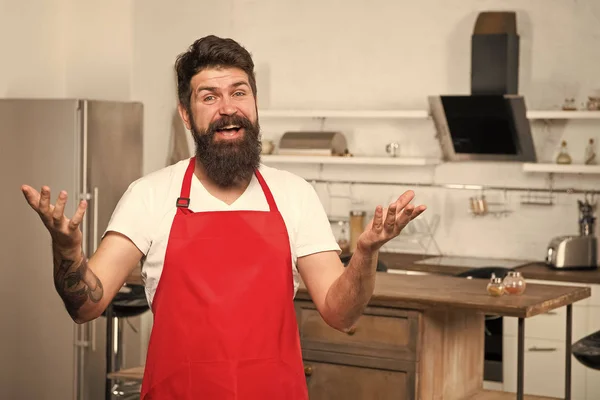 Cocinar en cocina nueva. Necesito inspiración culinaria. El fin de semana comienza con un delicioso desayuno. Cómo convertir la cocina en casa en hábito. Hombre barbudo delantal hipster rojo de pie en la cocina. Tienda de muebles de cocina —  Fotos de Stock