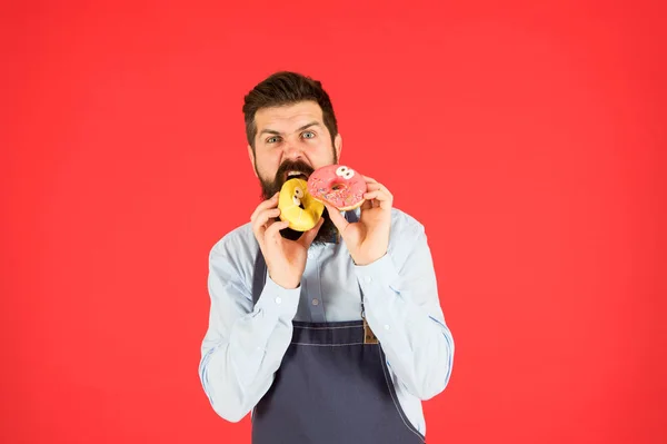 Hipster sakallı fırıncı çörek yiyor. Çörek fırını. Sakallı neşeli bakımlı adam çörek satıyor. Karbonhidrat ve kalori. Fırın sahibi. Fırın işi. Hamur işleri. Tatlılar ve kekler. Abur cubur — Stok fotoğraf