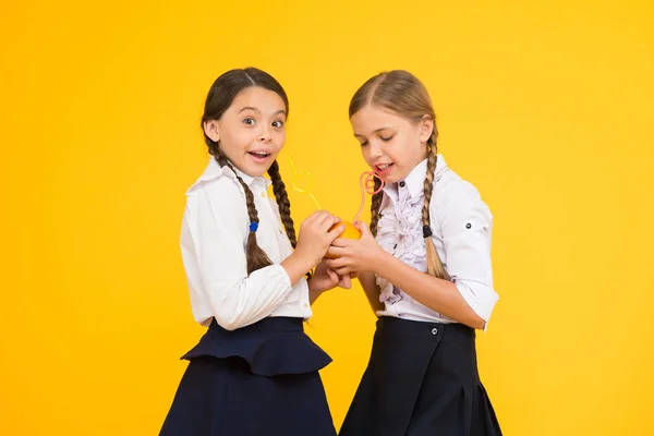 Witamina C jest kluczowa dla wzrostu. Małe dziewczynki piją sok witaminowy z owoców pomarańczy na żółtym tle. Małe dzieci w wieku szkolnym z zdrowego napoju witaminowego. Korzyści witaminy żywności — Zdjęcie stockowe