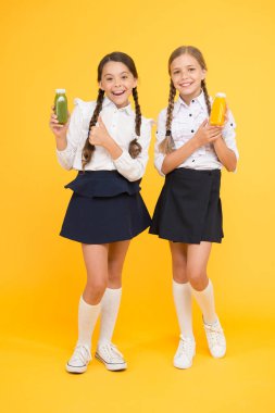 Sağlıklı beslenme. Kız öğrenciler sarı arka planda meyve suyu şişesi tutuyorlar. Okul zamanında susuzluğu gidermek. Susuzluk ve susuzluk. Sağlıklı snack meyve yüzlü. Smoothie detoksu. Nefis smoothie