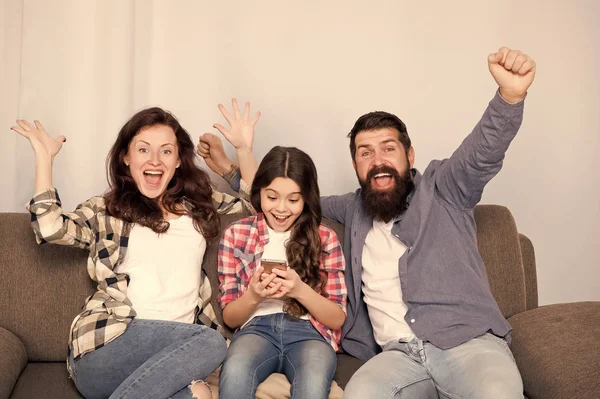 Niño niña utilizar el teléfono inteligente con los padres. Familia amigable divirtiéndose juntos. Mamá papá y la hija ocupada relajarse en el sofá. De ocio familiar. Asesoría parental. Familia pasar fin de semana juntos — Foto de Stock