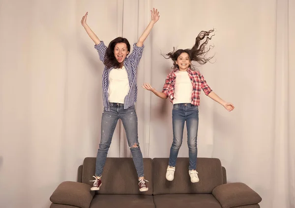 Girls only. Mom and daughter close friends. Mother and cheerful daughter having fun jumping couch. Happy childhood. Girls having fun. Fun leisure at home. Kid and mom play together. Happiness and fun