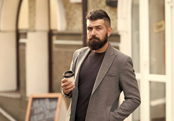 Drinking his cup first thing in the morning. Businessman in hipster style holding takeaway coffee. Hipster with disposable paper cup walking in city. Bearded man enjoying morning coffee. Coffee break