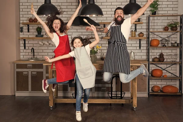 Having fun in kitchen. Family mom dad and little daughter wear aprons jump in kitchen. Family having fun cooking together. Teach kid cooking food. Weekend breakfast. Cooking with child might be fun