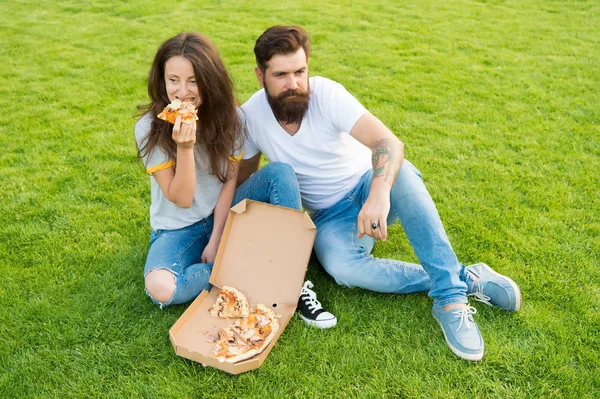 Simple happiness. Cheat meal. Couple eating pizza relaxing on green lawn. Fast food delivery. Bearded man and girlfriend enjoy cheesy pizza. Couple in love dating outdoors with pizza. Hungry people