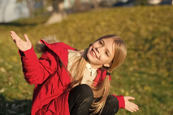 Sentez-vous heureux jour ensoleillé d'automne. Fille manteau heureux usure avec capuche profiter de la nature automne. Manteau enfant pour la saison d'automne. Vêtements d'automne et concept de mode. Enfant blonde cheveux longs marche automne parc arrière-plan — Photo