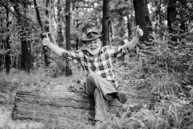 başparmak yukarı. mutlu ormancı. insan ve doğa. derin ahşap yürüyüş. orman sahibi. yaz veya bahar pikniği. kıdemli adam çiftçi ormanda dinlenmek. kovboy şapkalı sakallı olgun adam. çiftçi ahşap üzerinde oturup