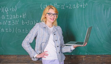 Modern dizüstü bilgisayarlı, internet karatahtasında sörf yapan zarif öğretmen. Uzaktan eğitim kavramı. Gözlük takan kadın öğretmen internette dizüstü bilgisayar tutuyor. Okul yeniliği kavramı