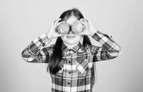 La magdalena, un regalo en miniatura. Graciosa niñita cubriendo los ojos con pasteles. Pequeño niño divirtiéndose con cupcakes. Chico juguetón horneando magdalenas en casa. Disfrutando de sabor favorito cupcake — Foto de Stock