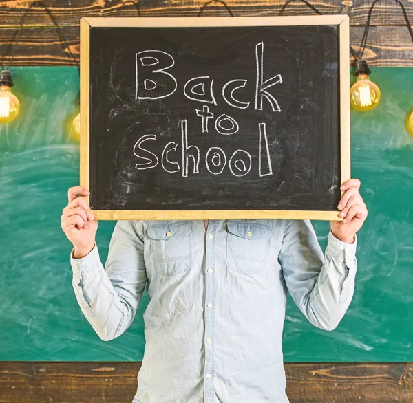 Concept de début d'année scolaire. Enseignant sans visage tient tableau noir avec titre de retour à l'école. Le professeur tient un tableau devant le visage. L'homme accueille les étudiants, tableau sur backgroun — Photo