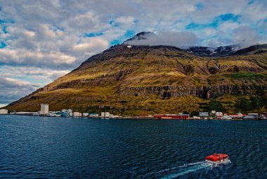İzlanda gezisi. Sejdisfjordur, İzlanda dağ manzarası denizde tekne float. Bulutlu gökyüzü dağda ile yalı. Su ile seyahat. Macera ve keşif. Yaz tatil ve yolculuk tutkusu