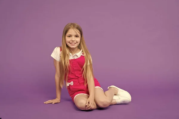 Tell me your story. Girl happy face sit on floor ready listen story violet background. Kid girl with long hair cute outfit relax wait interesting story. Child look fashionable. Story time concept