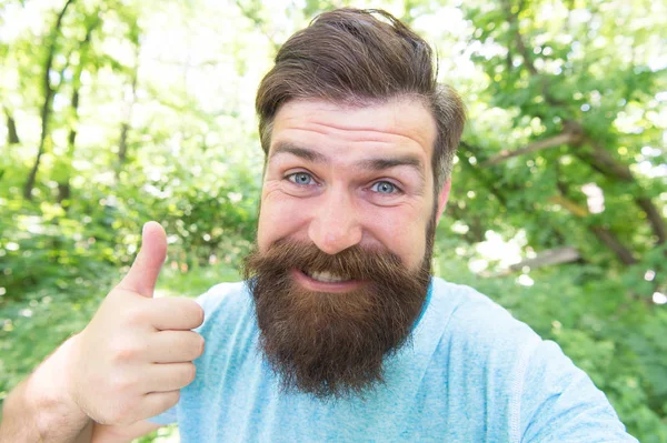 Dar um polegar ao barbeiro. Feliz barbeiro gesticulando na paisagem natural. Homem barbudo com barba em forma e cabelo bigode sorrindo antes ou depois de visitar o barbeiro. Uma barbearia apenas para homens — Fotografia de Stock