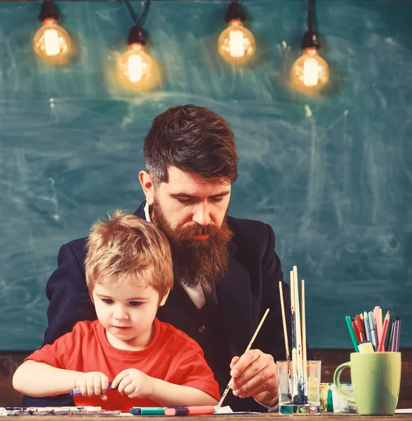 ひげを生やした教師、父と小さな息子が絵を描き、作成し、背景に黒板を描きながら教室で。忙しい顔の子供と教師は、絵画、描画。才能と創造性の概念 — ストック写真