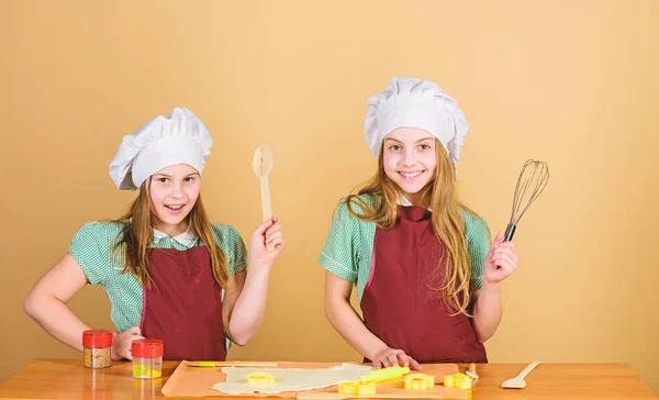 家族のレシピ。料理のスキル料理教育。生姜クッキーを焼く。女の子の姉妹は楽しい生姜生地を持っています。自家製クッキーが一番。子供たちは一緒にクッキーを焼きます。子供のエプロンとシェフの帽子の料理 — ストック写真