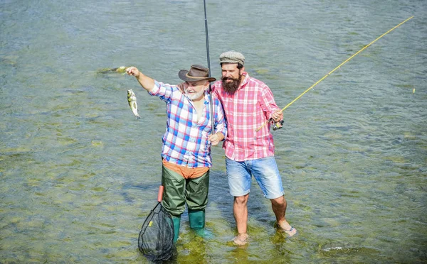 Os campeões jogam como um. hobby e atividade esportiva. Isca de truta. dois pescadores felizes com vara de pesca e rede. amizade masculina. ligação familiar. Fim de semana. homens maduros pescador. pai e filho pesca — Fotografia de Stock