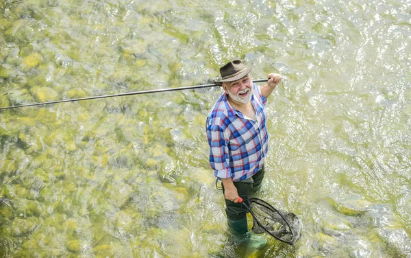 Summer leisure. Fisherman fishing equipment. Hobby sport activity. Fisherman alone stand in river. Fish normally caught in wild. Man bearded fisherman. Weekends made for fishing. Active sunny day