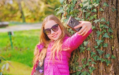 güzel selfie. küçük kız parkta boş zaman geçirmek. parkta mutlu çocuk. Yaz. Doğal güzellik. Çocukluk mutluluğu. telefonda selfie çekin. Yeşil çevre. sarmaşık yaprakları ile ağaç üzerinde tırmanma bitki