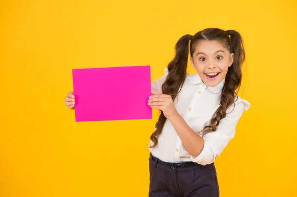 Okul mutlu bir yerdir. Sarı arka planda boş pembe kağıt tutan mutlu küçük çocuk. Küçük kız boş posterle gülümsüyor. Seni mutlu edecek, kopyalama alanı. — Stok fotoğraf