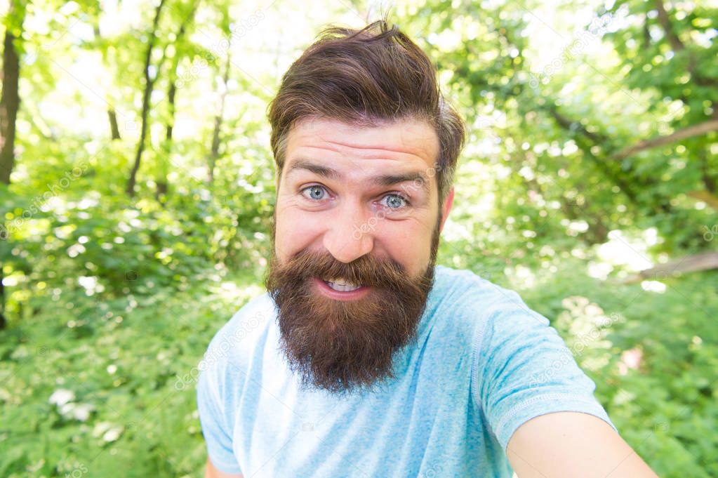 Beard can make a man look more brutal. Happy man with long mustache and beard hair outdoor. Brutal man smiling with unshaven face and stylish haircut. Bearded man in casual style on natural landscape